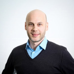 Ein professionelles Porträt eines Mannes in Business-Kleidung vor hellem Hintergrund.